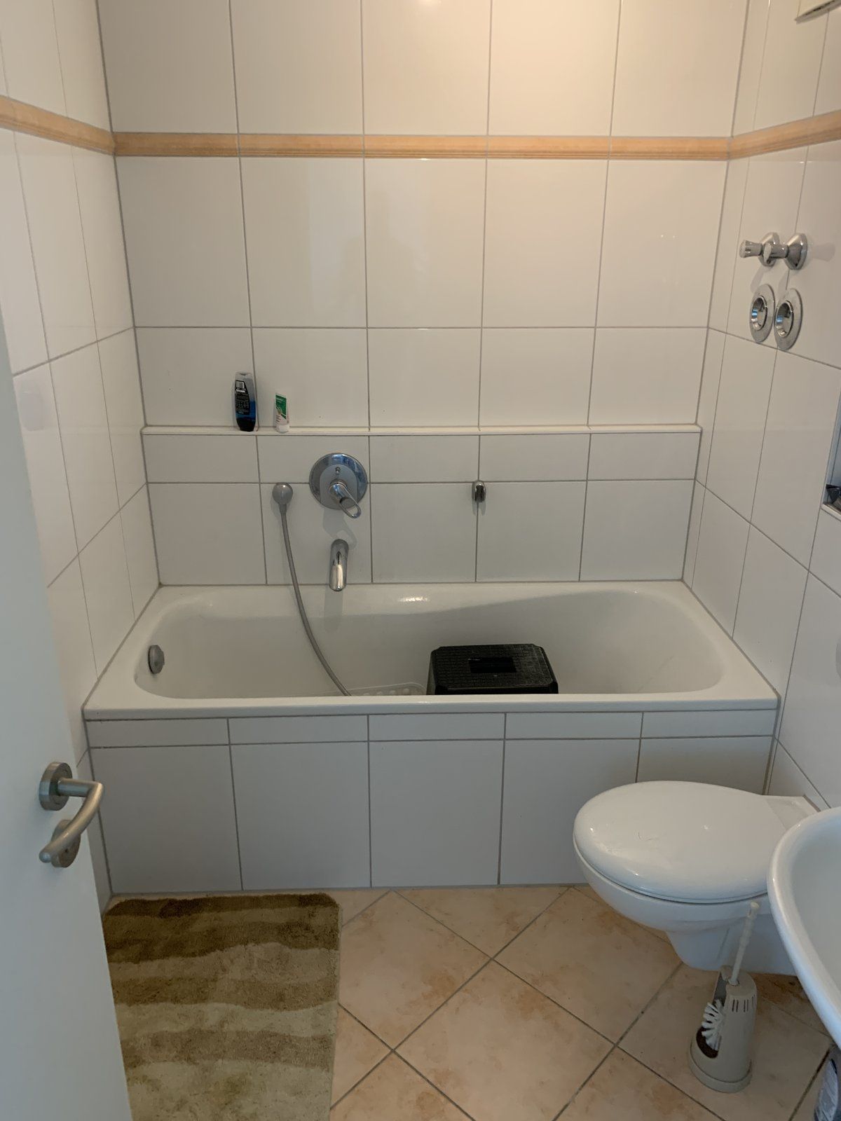 Vorher: Badewanne mit Hocker darin, weiße Fliesen