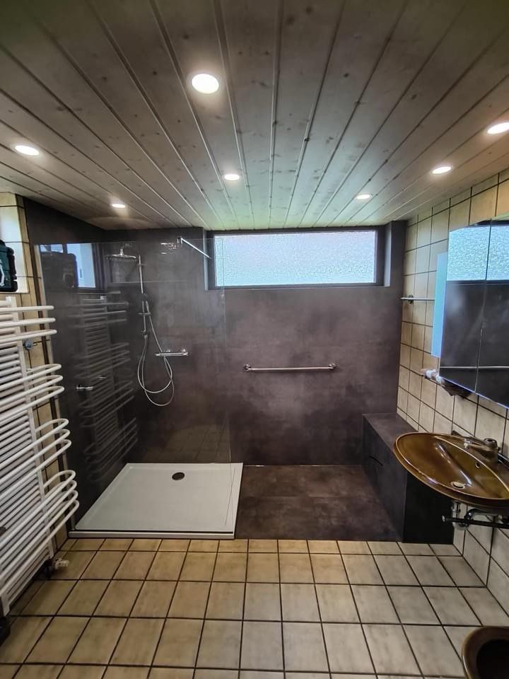 Nachher: große Dusche mit dunklen Wandpaneelen und Haltegriff